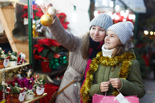 Smiling girl with woman are buying toys for X-mas tree in the market outdoor.