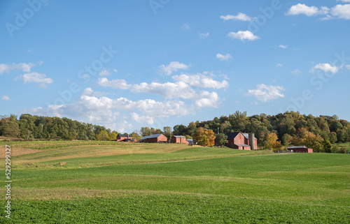 Amish farm buildings on a hill surrounded by fields and woods on a sunny day in Holmes County, Ohio, USA