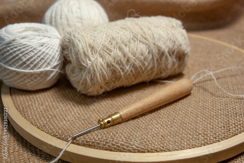 Punch needle with a burlap fabric in a embroidery hoop and a threaded needle with a woolen thread