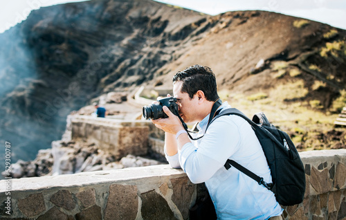 Close up of tourist man taking photos at a volcanic viewpoint. A tourist man with a photo camera taking photos at a viewpoint. Adventurous man with his camera taking photos at a viewpoint