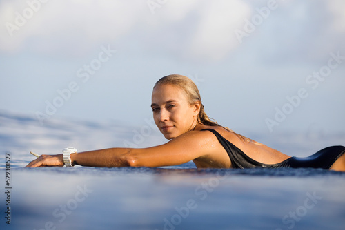 Portrait of confident woman lying on surfboard at beach against sky