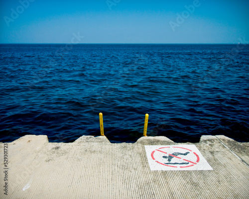 No swimming sign on pier over sea against clear blue sky