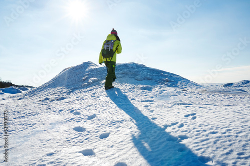 Rear view of female hiker walking on snow covered field against sky photo