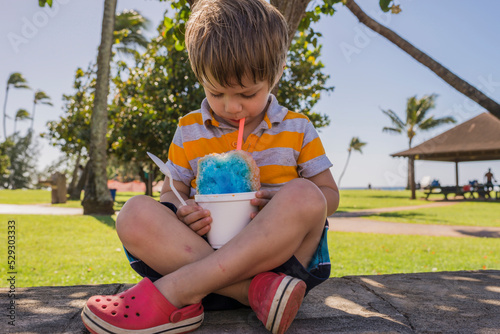Boy eating slush while sitting on footpath at park