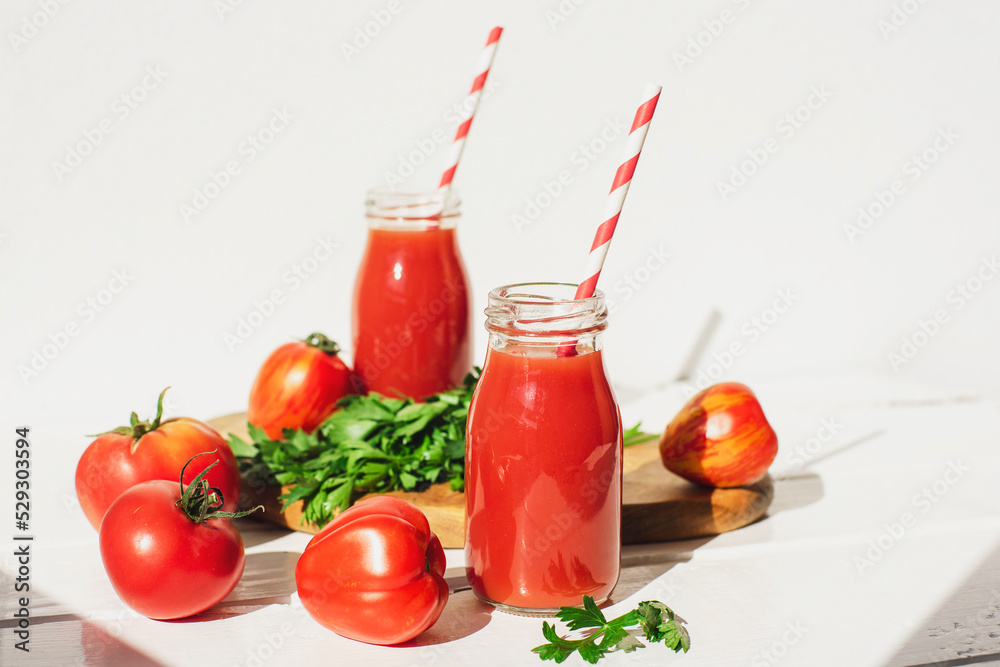 Tomato juice in bottles and fresh red tomatoes on a white wooden table. Healthy vegan food. Close-up, selective focus Tomato juice in bottles and fresh red tomatoes on a white wooden table. Healthy vegan food. Close-up, selective focus