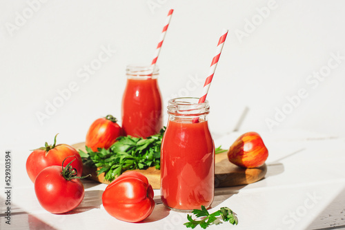 Tomato juice in bottles and fresh red tomatoes on a white wooden table. Healthy vegan food. Close-up, selective focus