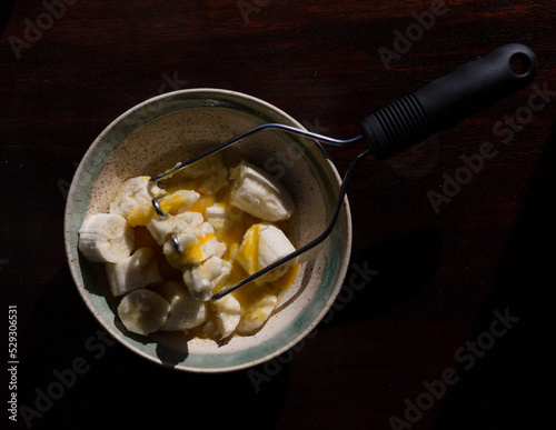 Overhead view of banana slices and eggs in bowl with masher on table