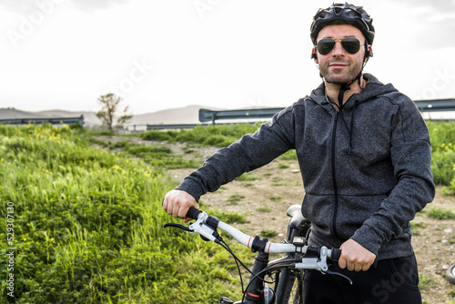 Portrait of man with bicycle standing on field against clear sky