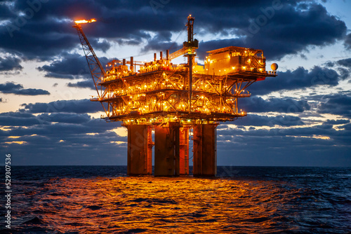 Illuminated oil exploration platform in sea against cloudy sky during sunset photo