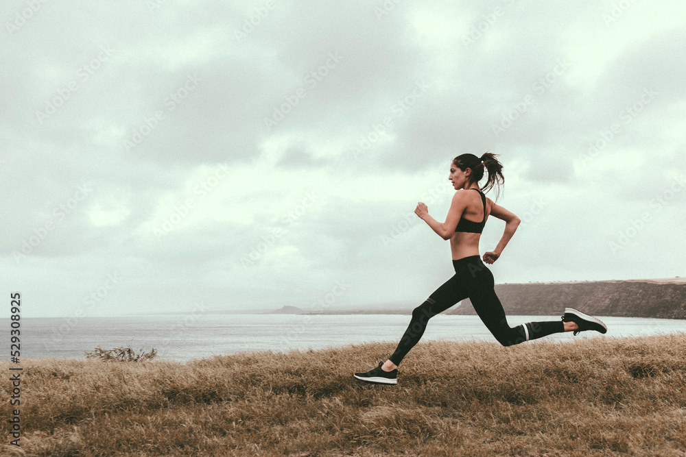 Woman running on grassy field by sea against cloudy sky Woman running on grassy field by sea against cloudy sky
