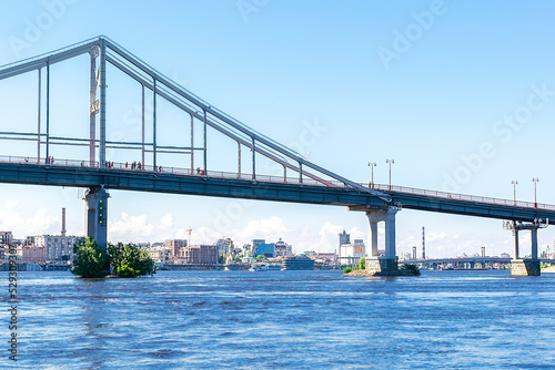 Scenic nature travel cityscape river Dnipro with blue water and metal pedestrian bridge at sunny summer day in Kiev. View from inside river, ship on water-Kiev Ukraine