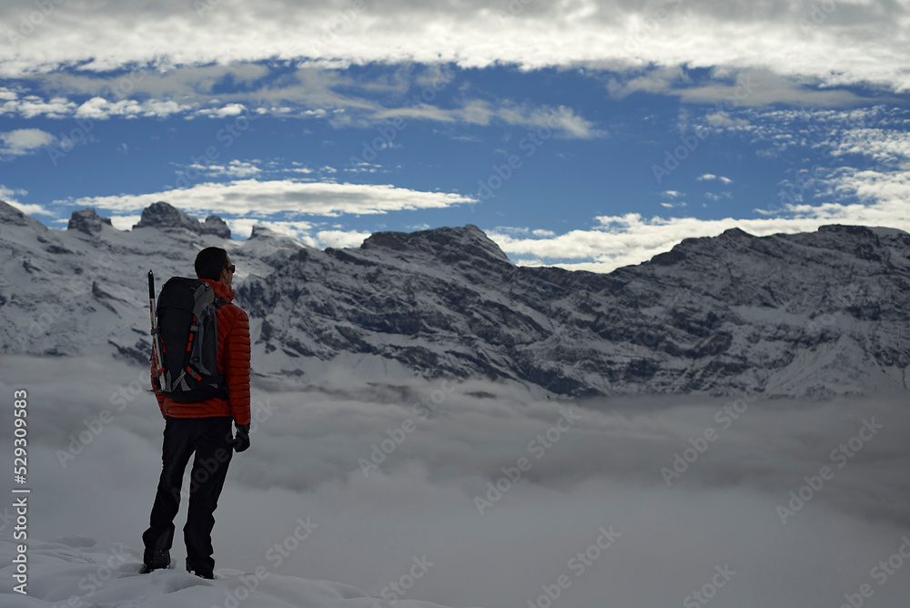 Rear view of hiker with backpack looking at mountain ranges against cloudy sky during winter Rear view of hiker with backpack looking at mountain ranges against cloudy sky during winter