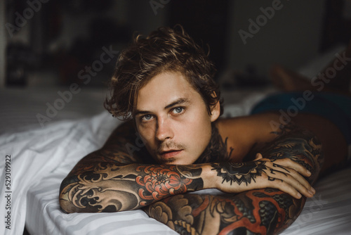 Portrait of shirtless tattooed man lying on bed at home photo