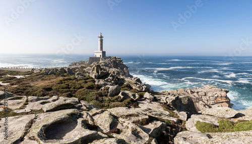 Punta Nariga Lighthouse on rocks by sea against clear blue sky during sunny day