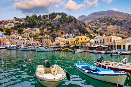 Fotografiet View on Symi (Simi) island harbor port, classical ship yachts, houses on island hills, Aegean Sea bay