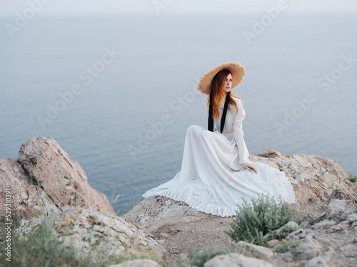 Woman looking away while sitting on rock formation against sea during sunset photo