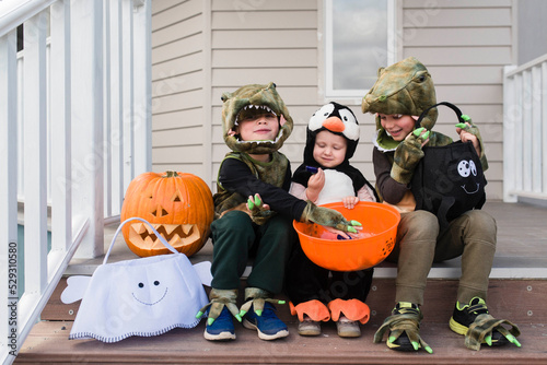 Happy siblings in Halloween costumes sitting on steps against house photo