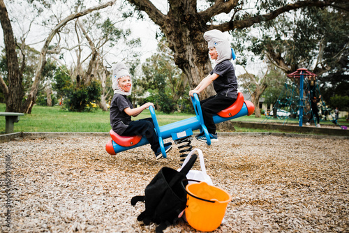 Brothers wearing shark costumes while playing seesaw at playground during Halloween photo