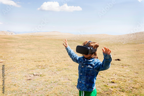 Boy looking through virtual reality simulator while standing on landscape against sky during sunny day