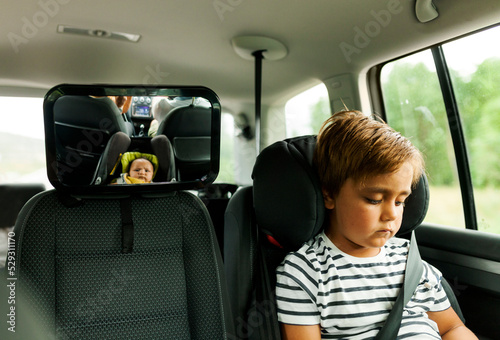 Brother sitting on car seat while sister reflecting in mirror photo