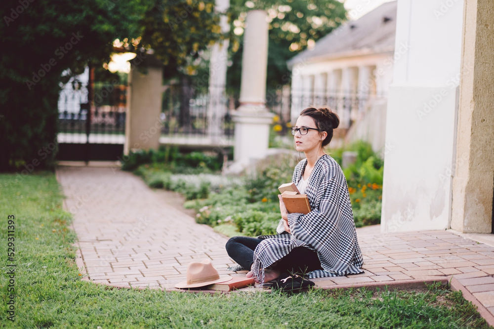Thoughtful woman with books looking away while sitting in yard