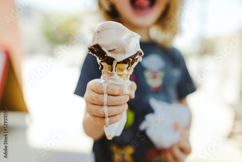Midsection of boy holding melting ice cream cone while standing outdoors photo