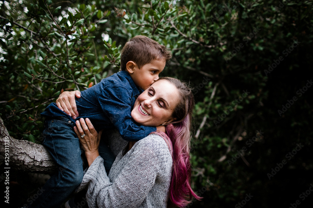 Son kissing mother while sitting on tree at park Son kissing mother while sitting on tree at park