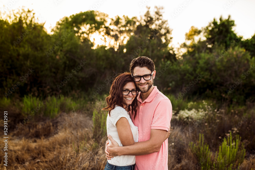 Portrait of happy couple embracing while standing on field during sunset Portrait of happy couple embracing while standing on field during sunset