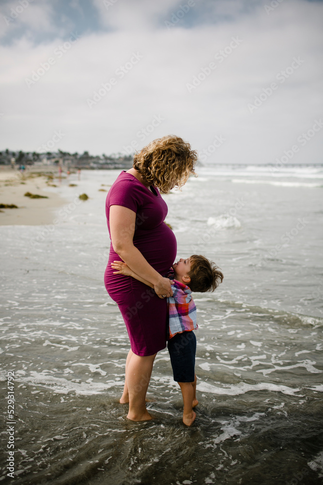 Side view of pregnant mother with son standing in sea against cloudy sky Side view of pregnant mother with son standing in sea against cloudy sky