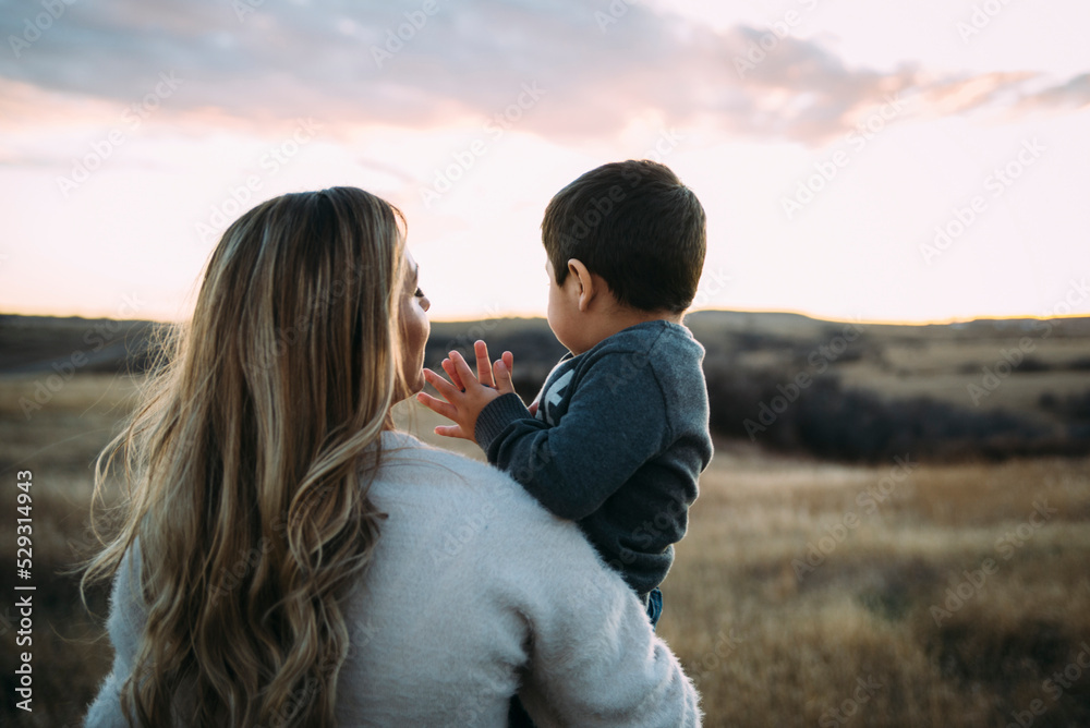 Rear view of mother carrying son on field during sunset Rear view of mother carrying son on field during sunset