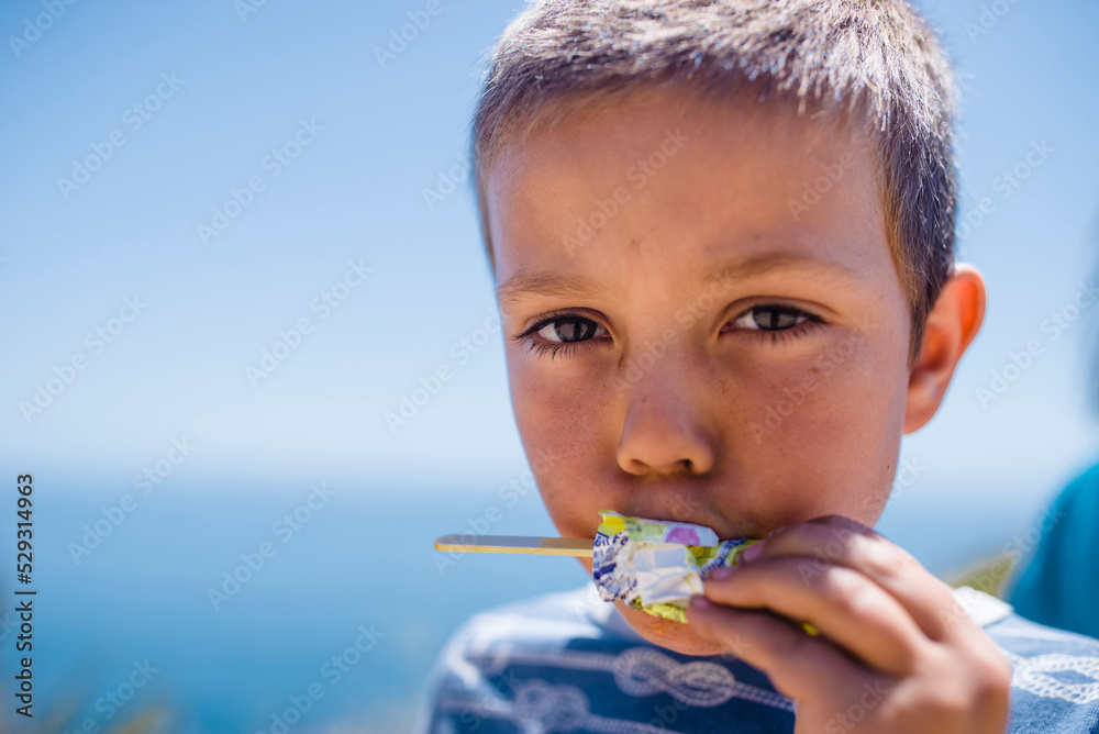 Portrait of boy eating flavored ice against sea and sky during sunny day Portrait of boy eating flavored ice against sea and sky during sunny day