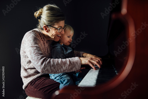 Side view of grandmother and grandson playing piano at home photo