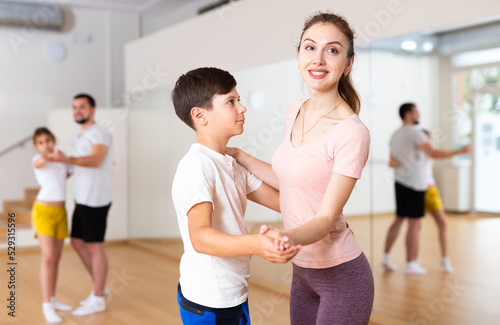 Young woman practicing active dance in pair with her tween son during family dance class