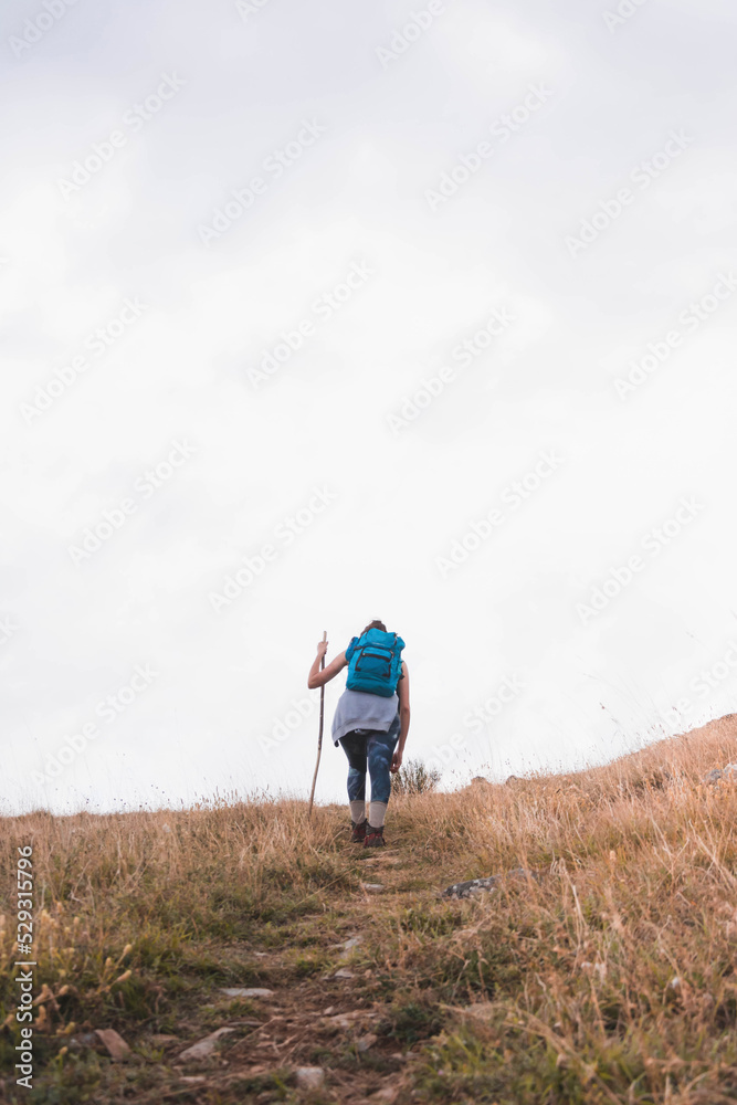 Low angle view of female hiker with backpack walking on grassy mountain against sky Low angle view of female hiker with backpack walking on grassy mountain against sky