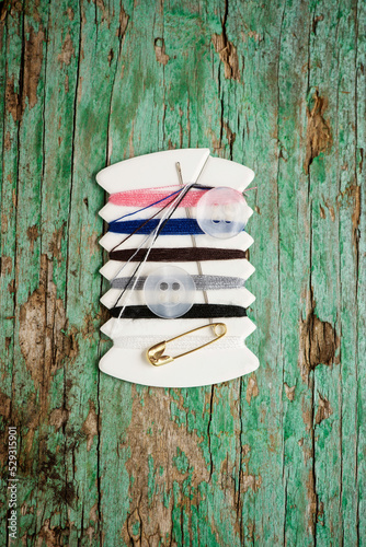 Overhead view of colorful threads with buttons and needle on wooden table
