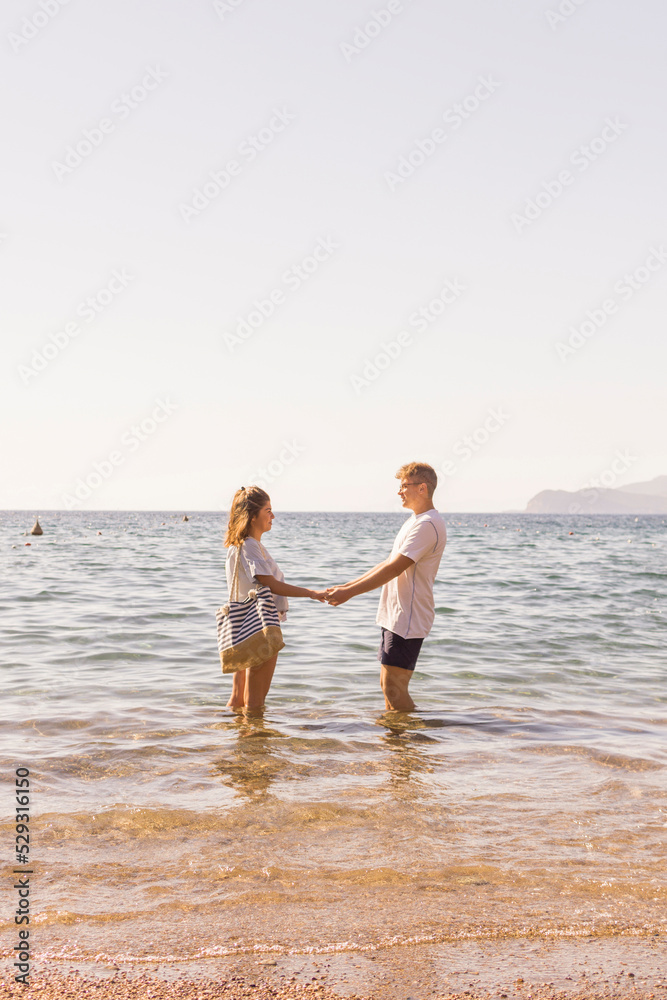 Side view of young couple holding hands while standing in sea against clear sky Side view of young couple holding hands while standing in sea against clear sky