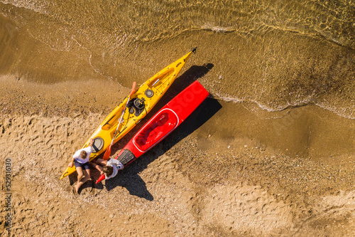 High angle view of young couple sitting on kayaks at beach during sunny day photo