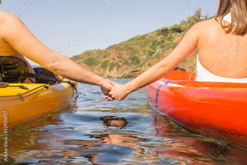 Midsection of young couple holding hands while sitting in kayaks on sea against clear sky photo