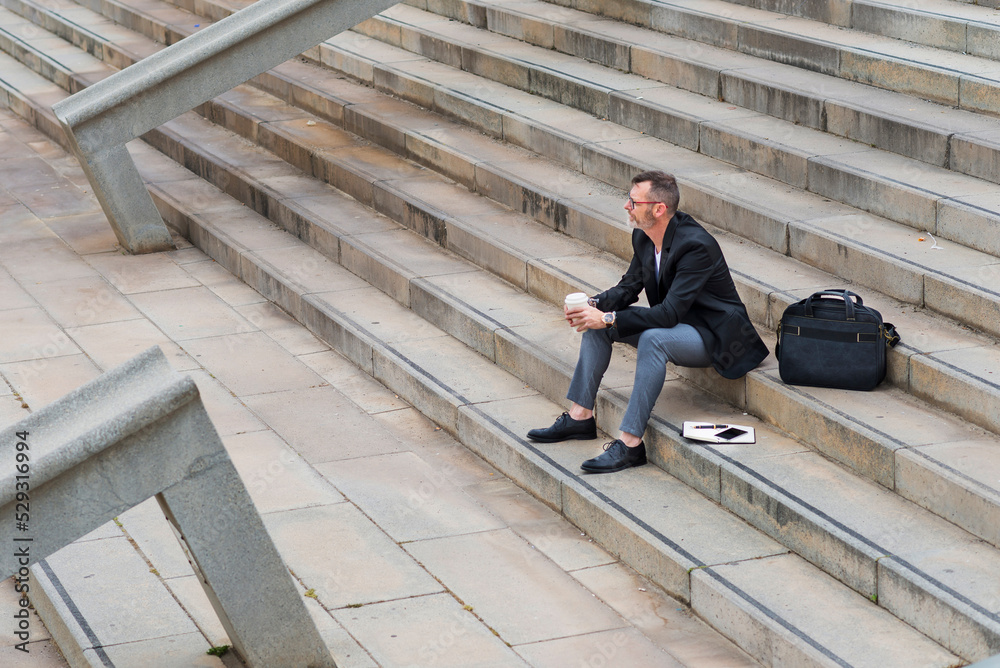 High angle view of thoughtful businessman holding coffee while sitting on steps in city High angle view of thoughtful businessman holding coffee while sitting on steps in city