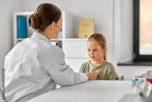 medicine, healthcare and pediatry concept - female doctor or pediatrician with stethoscope and little girl patient on medical exam at clinic