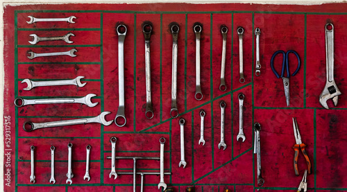 Various wrenches with pliers and scissors arranged on red wall in workshop photo