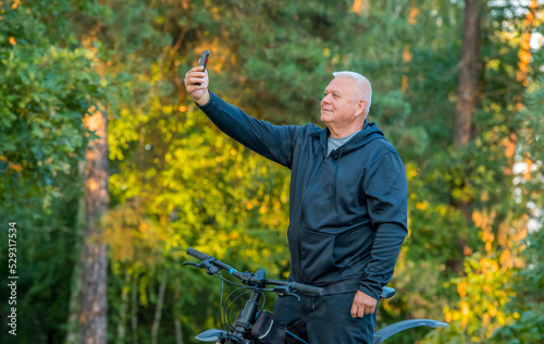 an elderly sports man uses a smartphone while walking on a bicycle