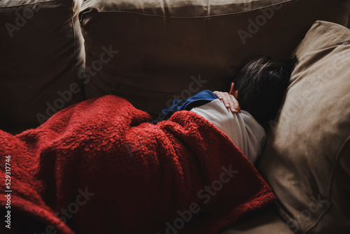 Young boy sleeping on a couch under a blanket facing away