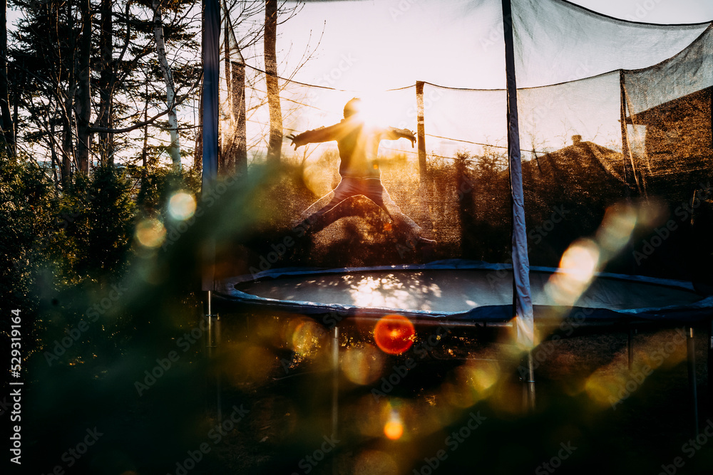 young boy jumping on trampoline in a star position during golden hour Stock  Photo | Adobe Stock