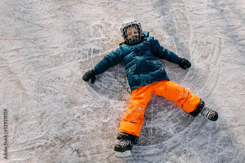 boy making angel on outdoor ice rink as he fell while skating