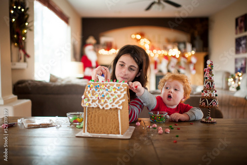 Two kids decorating a gingerbread house for the holidays at home photo