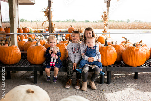 Four siblings sitting among pumpkins at store photo