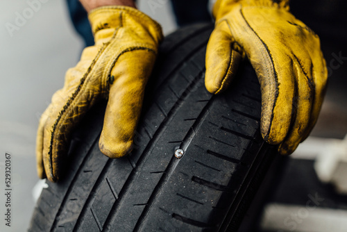 Dirty yellow leather mechanic gloves holding car tire with nail in it photo