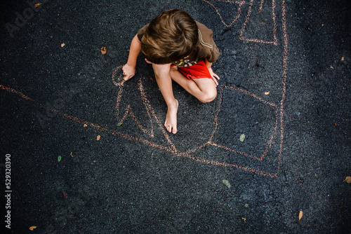 young boy drawing on driveway with chalk, seen from above photo