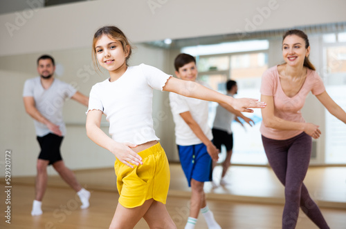 Portrait of positive pre-teen girl doing dance workout with her brother and parents during family class